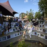 Bestival 2025 Teilnehmende sitzen im Holzmarkt 25 auf einer Holzplattform mit verschiedenen Ebenen, welche mit Fotos diversen weiblichen Künstlerinnen bedruckt ist 