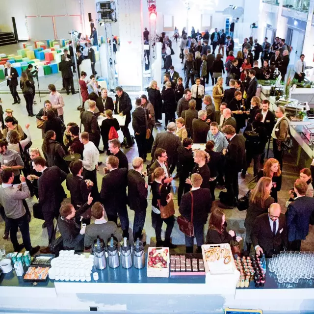 Menschenmenge aus Eventteilnehmenden in schicker Kleidung vor Büffet aus Vogelperspektive