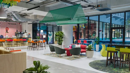Modernes, bunt eingerichtetes Büro mit Sitzbereichen, Pflanzen und großen Fenstern.