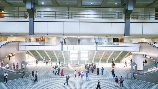 Spacious modern atrium with people walking and gathering on a tiled floor.