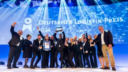 A group stands cheering in front of a screen that reads: German Logistics Award 2024