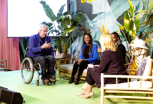 Four people have a discussion onstage with tropical plants in the background.
