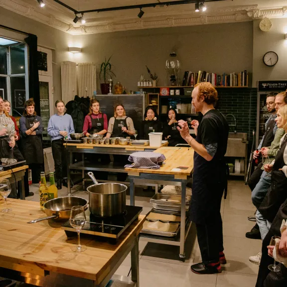 Kochkurs mit mehreren Teilnehmern in einer modernen Küche, Koch spricht zur Gruppe.