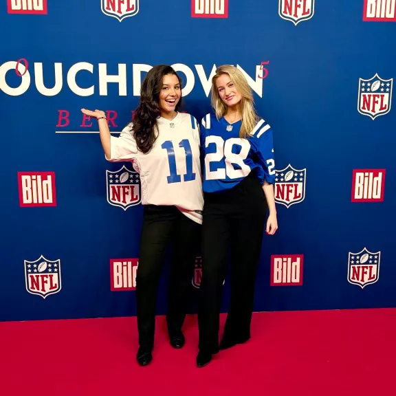 Zwei Frauen in NFL Trikots vor einem roten Teppich- Eventpersonal in Berlin.