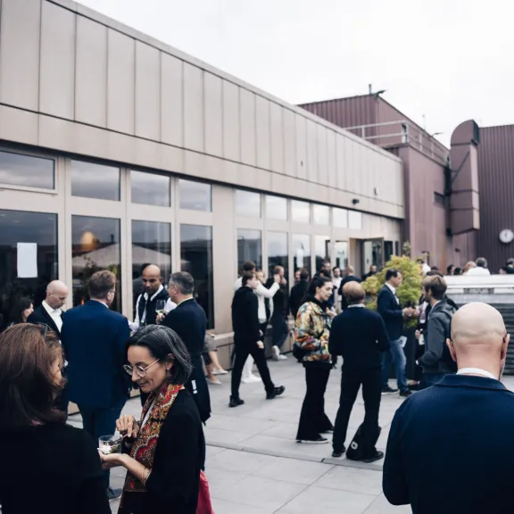 Menschen in formeller Kleidung unterhalten sich auf einer Dachterrasse.