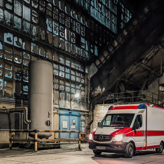 Krankenwagen steht nachts in einer alten, verlassenen Industriehalle.