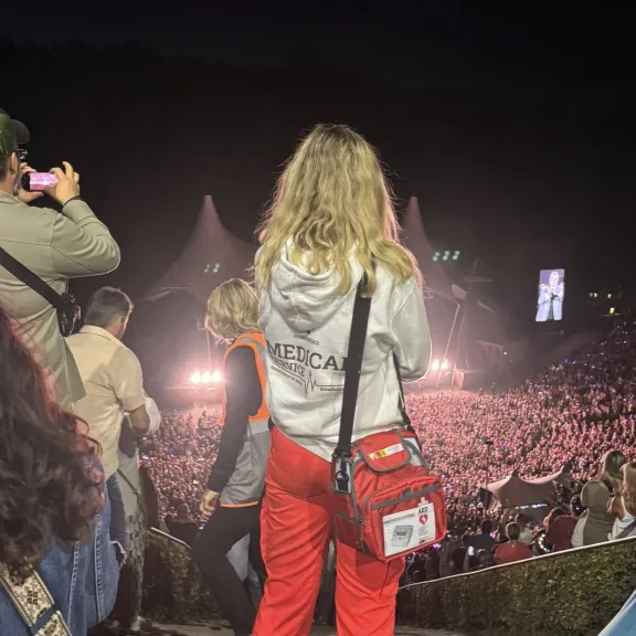 Sanitäterin mit roter Hose blickt auf eine große, beleuchtete Konzertbühne im Freien.