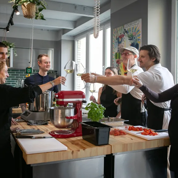 Gruppe von Menschen stößt in moderner Küche mit Weingläsern an.