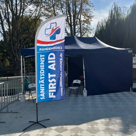 Erste-Hilfe-Zelt im Freien mit blauem Banner und Stühlen davor.
