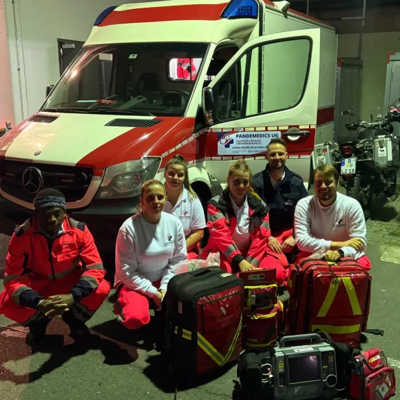 Sechs Rettungskräfte in Uniform vor einem Krankenwagen und Notfallausrüstung.