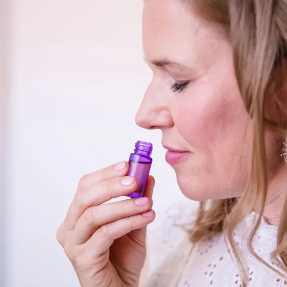 Frau hält lila Fläschchen unter die Nase und riecht daran, Augen geschlossen.
