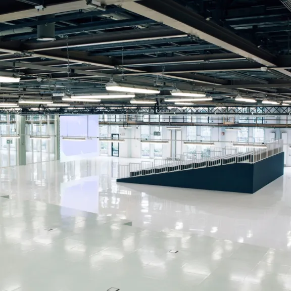 Große, leere Halle mit glänzendem weißen Boden und industrieller Decke.