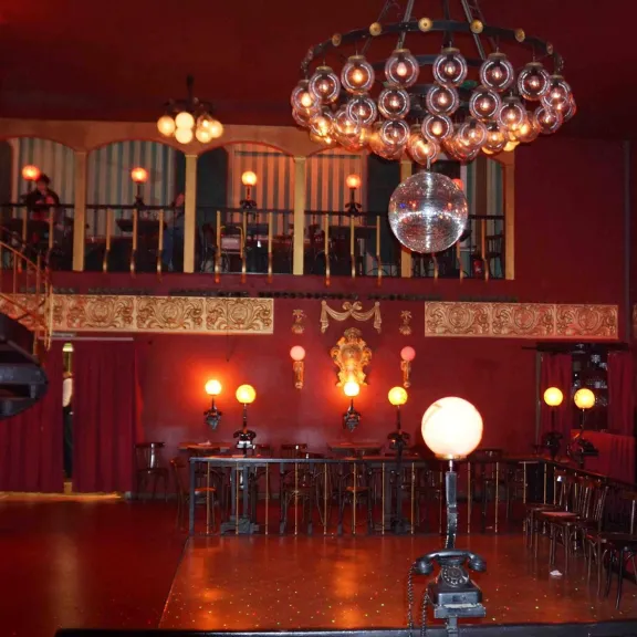 Roter Saal mit Kronleuchter, Bar, Bühne und Galerie, warm beleuchtet