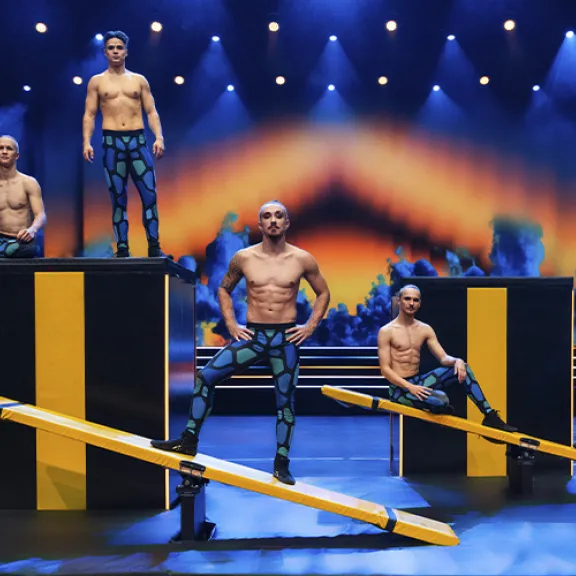 Fünf Akrobaten auf einer Bühne mit Turngeräten und bunten Lichtern.