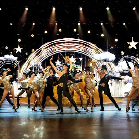 Viele Tänzer in glitzernden Kostümen auf einer festlich beleuchteten Bühne