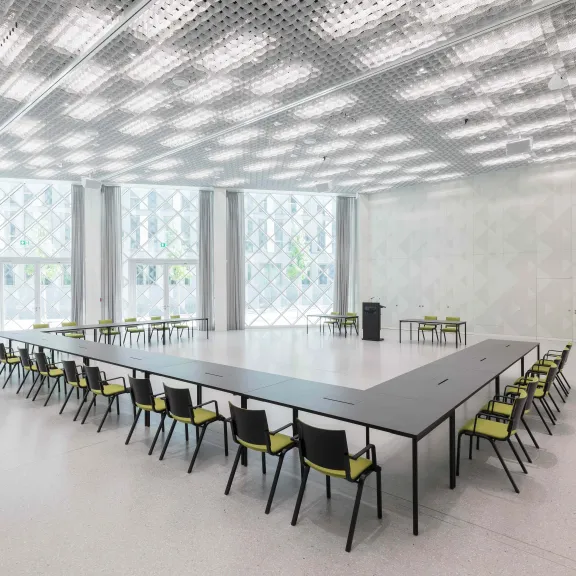 Großer heller Konferenzraum mit U-förmigem Tisch und vielen Stühlen.