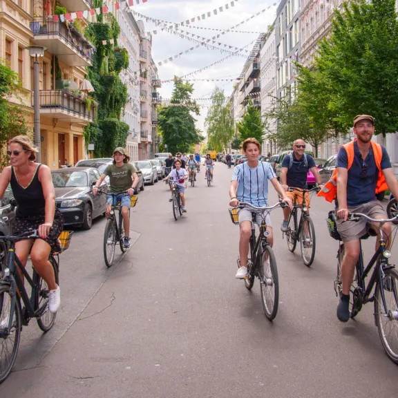 Mehrere Menschen fahren entspannt mit dem Fahrrad durch eine städtische Straße.