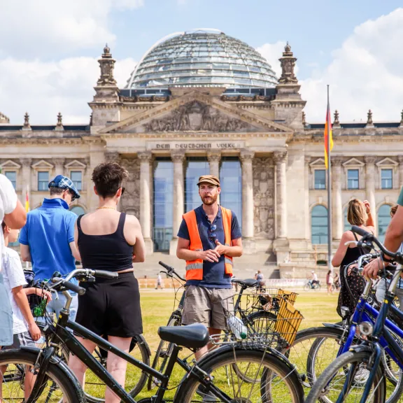 Gruppe von Radfahrern vor dem Reichstagsgebäude in Berlin bei sonnigem Wetter.