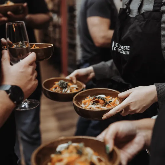Mehrere Personen halten Schalen mit Essen, eine Person hält ein Weinglas.