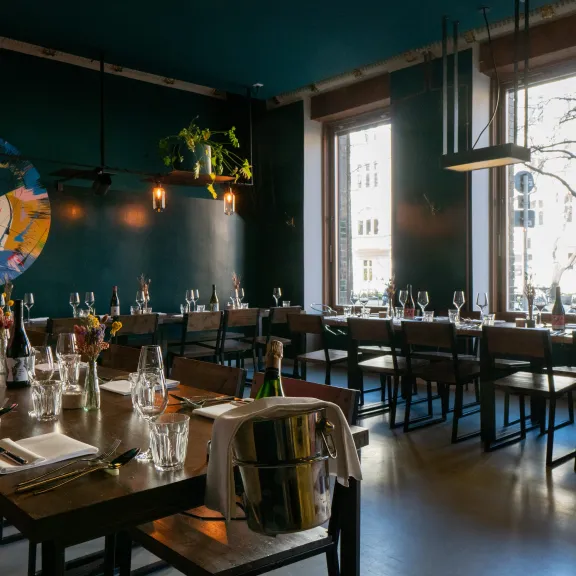 Modernes Restaurant mit gedeckten Tischen, großen Fenstern und dunkler Wandfarbe.