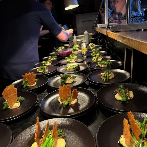 Koch richtet mehrere elegante Vorspeisen auf schwarzen Tellern in einer Restaurantküche an.