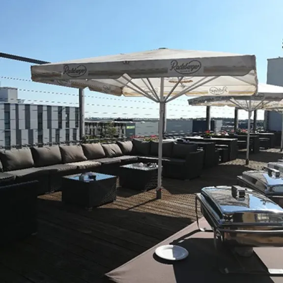Dachterrasse mit Sitzgruppen, Sonnenschirmen und Buffet bei Sonnenschein