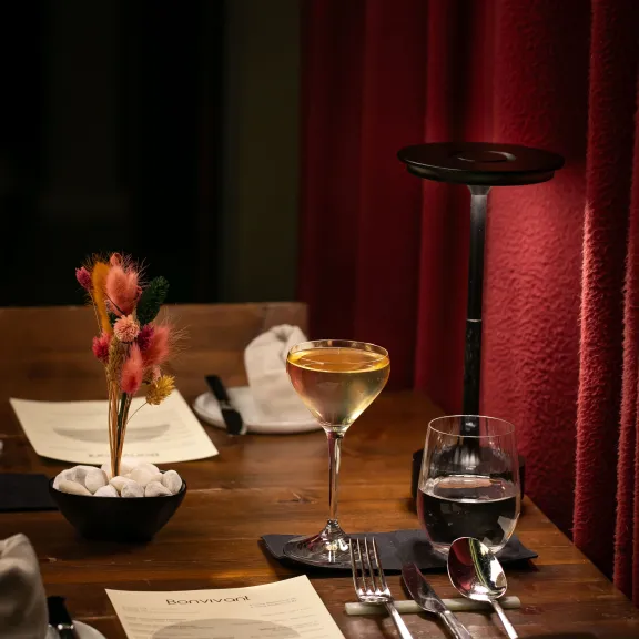 Elegant gedeckter Tisch mit Getränken, Speisekarte, Besteck und rotem Vorhang im Hintergrund.