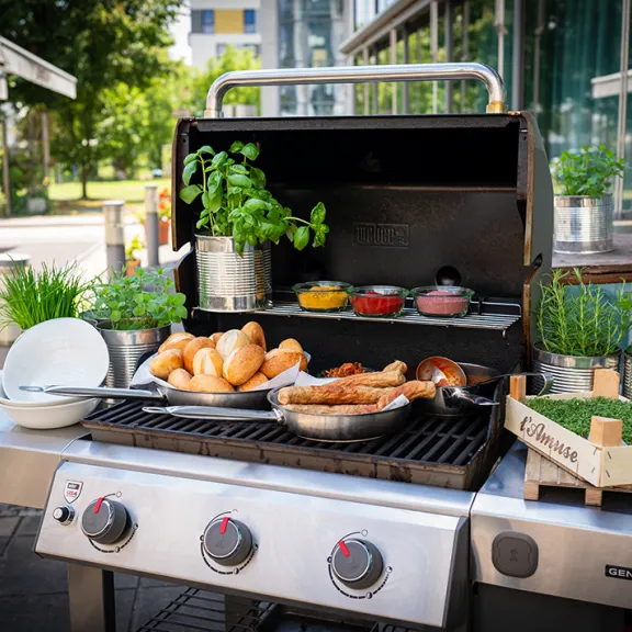 Eisstockpaket Sommer mit Grill & Würstchen, Brötchen, frischen Kräutern und Saucen im Freien.