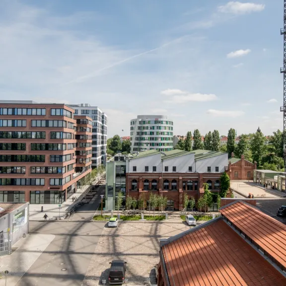 Moderne Bürogebäude und ein Gasometer bei sonnigem Wetter, grüne Bäume im Hintergrund.