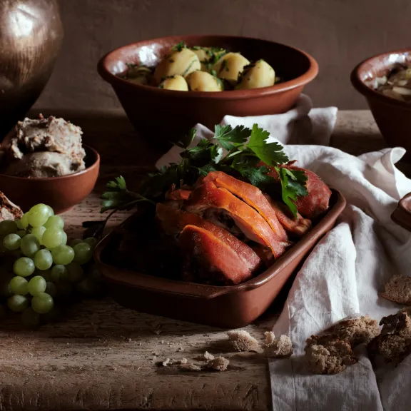 Rustikales Essen mit gebratenem Fleisch, Brot, Kartoffeln, Trauben und Gemüse in Tonschalen.