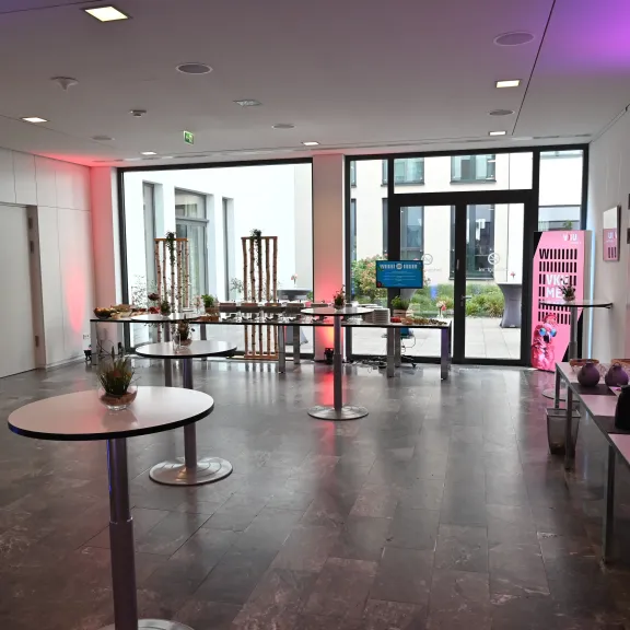 Heller Konferenzraum mit Stehtischen, Snacktisch und pinker Beleuchtung