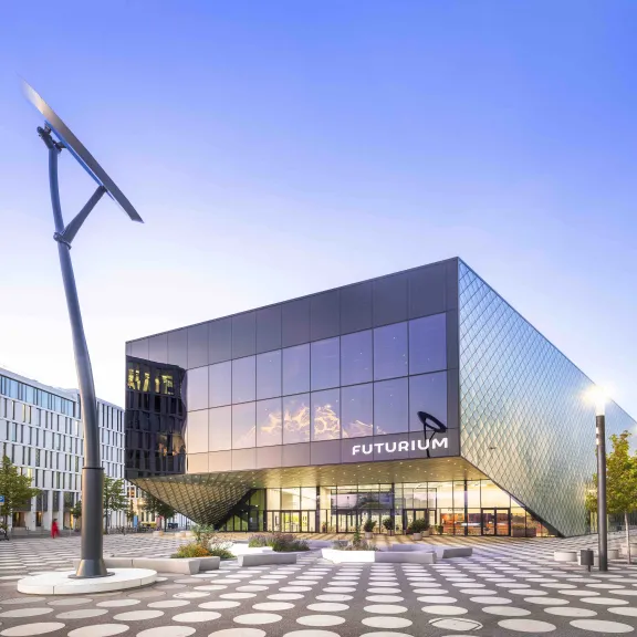 Modernes, kantiges Gebäude mit Glasfassade und großem Solarmodul auf dem Vorplatz