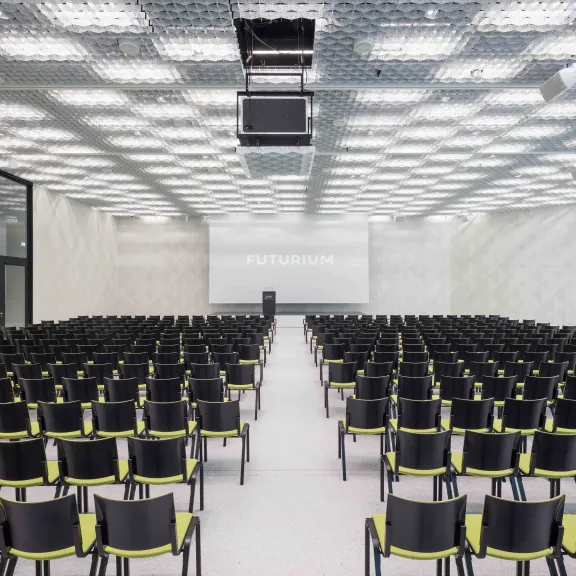 Leerer moderner Vortragssaal mit vielen schwarzen Stühlen und einer großen Leinwand vorne.