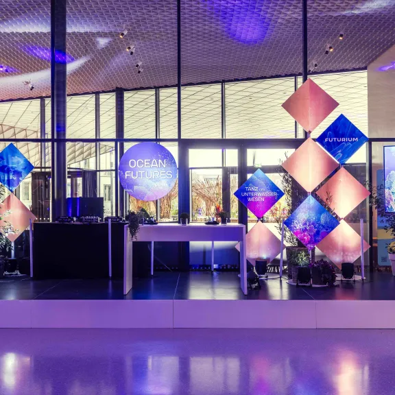 Bunt beleuchtete Bühne mit geometrischen Dekoelementen und Pflanzen in modernem Raum.