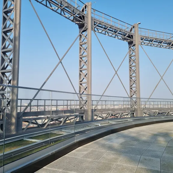 Stahlkonstruktion mit Glasgeländer, darunter Stadt im Hintergrund, blauer Himmel.