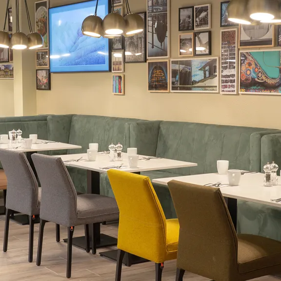 Gemütliches Café mit bunten Stühlen, grüner Bank und dekorierten Wänden.