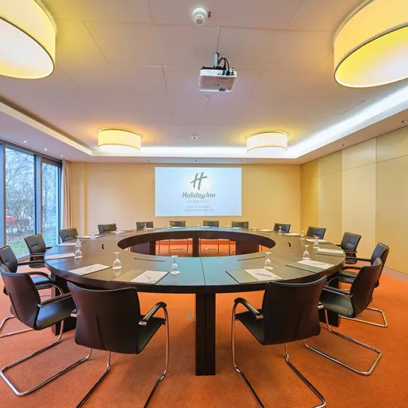 Moderner Konferenzraum mit ovalem Tisch, Stühlen und großem Bildschirm.