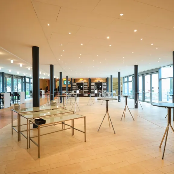 Heller, leerer Veranstaltungsraum mit Glastischen und Barhockern.