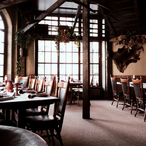 Gemütliches, rustikales Restaurant mit Holztischen und großen Fenstern.