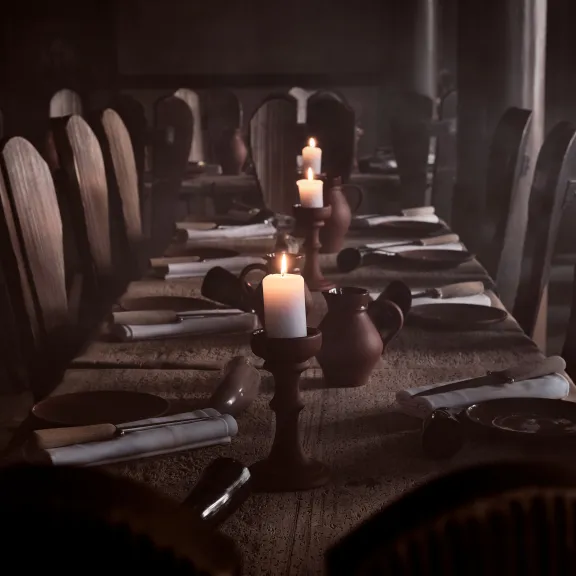 Langer Holztisch mit Kerzenlicht, eingedeckt für ein Abendessen, rustikale Atmosphäre.