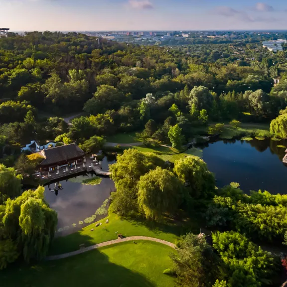 Großer Park mit Teich, Bäumen und Häusern, im Hintergrund eine weite Stadtlandschaft.