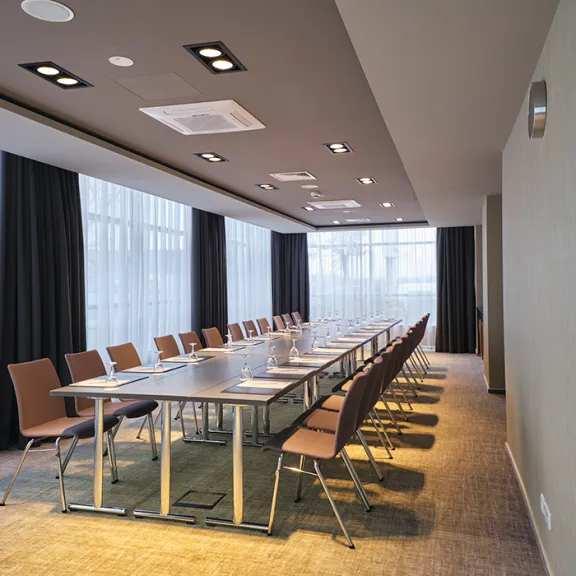 Moderner Konferenzraum mit langem Tisch, braunen Stühlen und großen Fenstern.