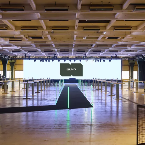 Großer, moderner Konferenzsaal mit Bühne, Lichtern und Begrüßungsbildschirm.