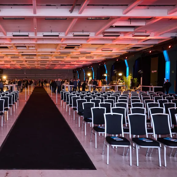 Großer Konferenzsaal mit vielen leeren Stuhlreihen und bunter Deckenbeleuchtung.