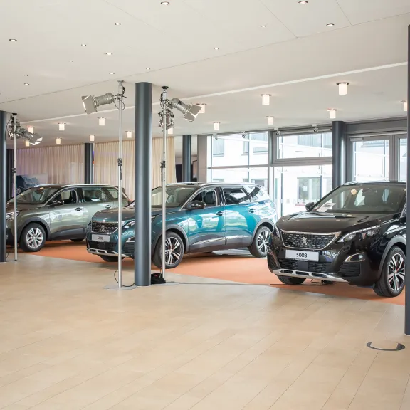 Drei Autos stehen in einem hellen Autohaus auf orangenen Teppichen.
