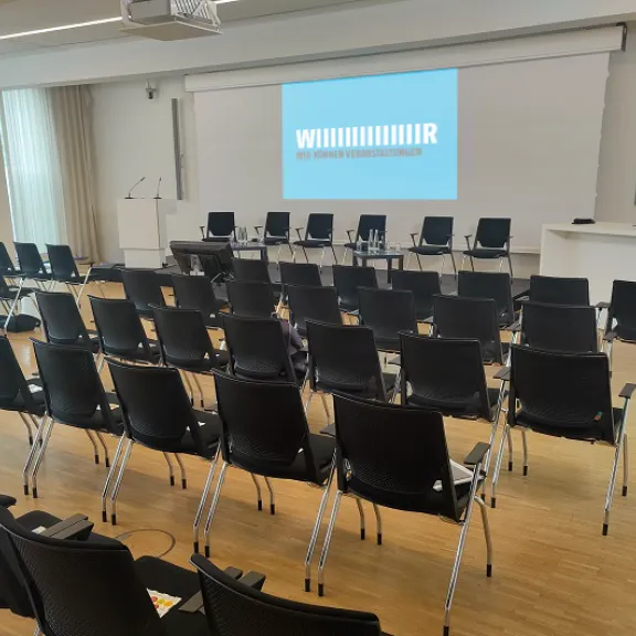 Leerer Konferenzraum mit schwarzen Stühlen und Bühne mit Leinwand.