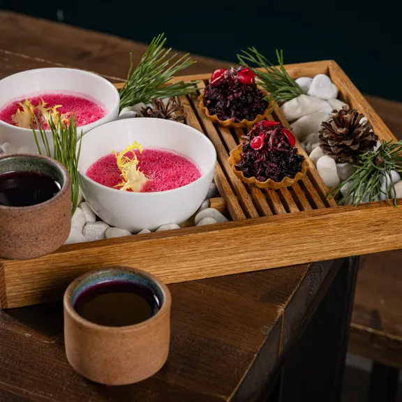 Holztablett mit zwei Suppenschalen, Deko aus Zapfen, Beeren, Zweigen und zwei Tassen.