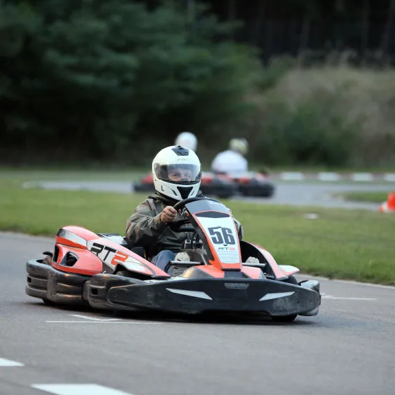 Person fährt mit Go-Kart auf einer Rennstrecke, weitere Fahrer im Hintergrund.
