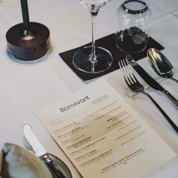 Weiß gedeckter Restauranttisch mit Besteck, Weinglas und Menükarte.