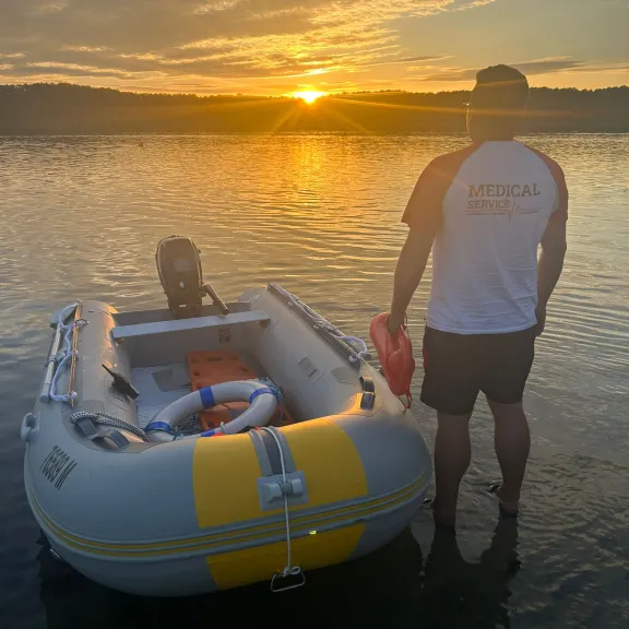 Mann steht neben Schlauchboot im seichten Wasser bei Sonnenuntergang.